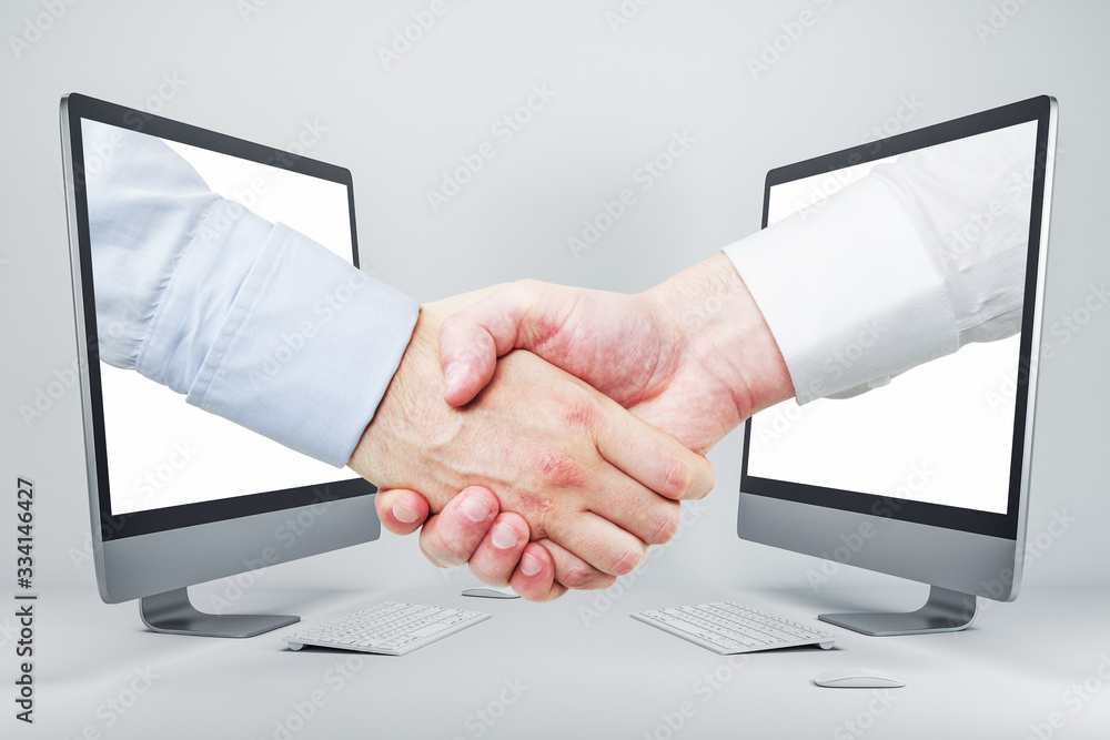 Businessmen shaking hands through computer screens Businessmen shaking hands through computer screens