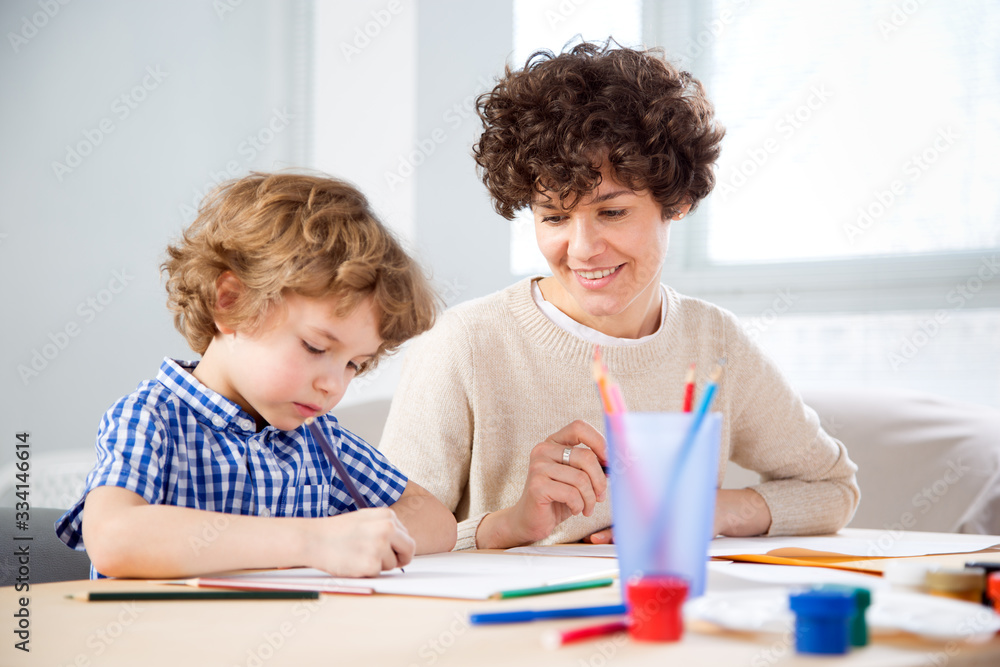 Happy mother and baby son drawing together in a room lit by the sun Happy mother and baby son drawing together in a room lit by the sun