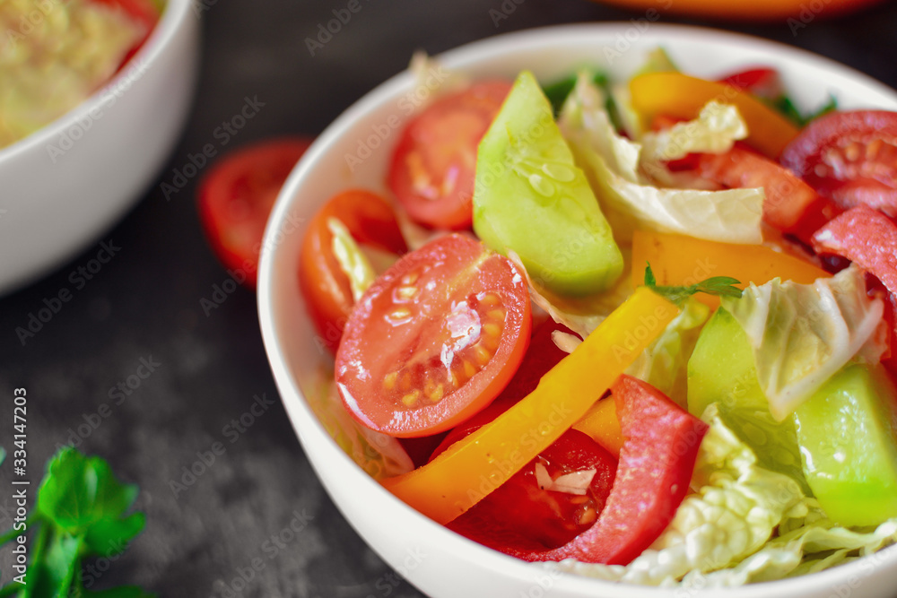 Spring vegetable salad. Salad, tomatoes, cabbage, dressing, bell pepper, cucumber, parsley. Dark background, top view. Close up. Spring vegetable salad. Salad, tomatoes, cabbage, dressing, bell pepper, cucumber, parsley. Dark background, top view. Close up.