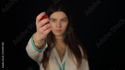 A young girl in medical gown clothing looking and pointing to the camera a model of coronavirus COVID-19 model. Dark background. Isolated. photo