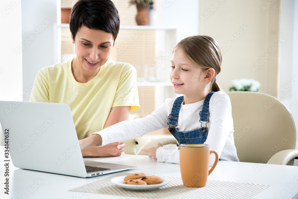 Woman and her little daughter are using a laptop and smiling