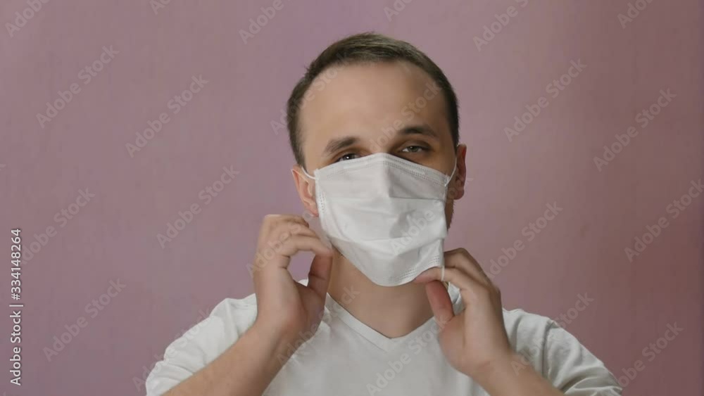Man puts on mask against covid 19, looks at camera and holding a poster. Coronovirus preventions. Pandemic. Global spread of coronavirus. Epidemic precautions. Acute Respiratory Man puts on mask against covid 19, looks at camera and holding a poster. Coronovirus preventions. Pandemic. Global spread of coronavirus. Epidemic precautions. Acute Respiratory