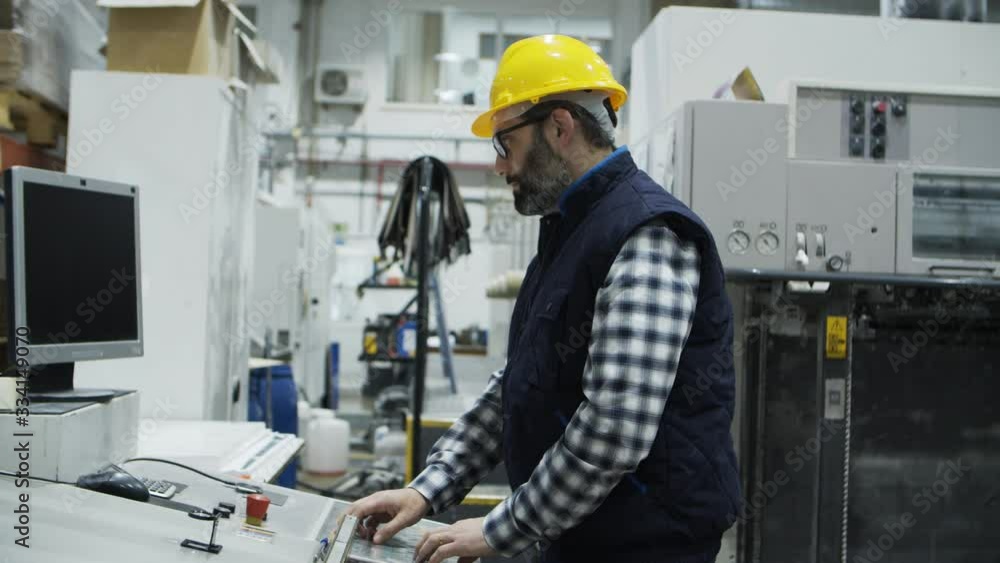 Side view of concentrated male worker setting printing machine. Focused technician working with printing machine. Manufacturing concept Side view of concentrated male worker setting printing machine. Focused technician working with printing machine. Manufacturing concept