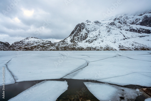 Snow covered mountains with icy lake infront in Lofoten, Norway. Snowy weather and overcast evening.
