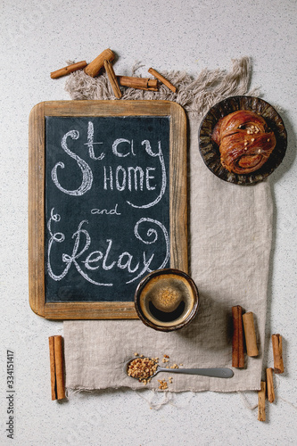 Traditional Swedish cinnamon sweet buns Kanelbulle on vintage tray, cup of coffee on linen cloth, chalkboard handwritten lettering Stay home and relax. White texture background, flat lay, space photo