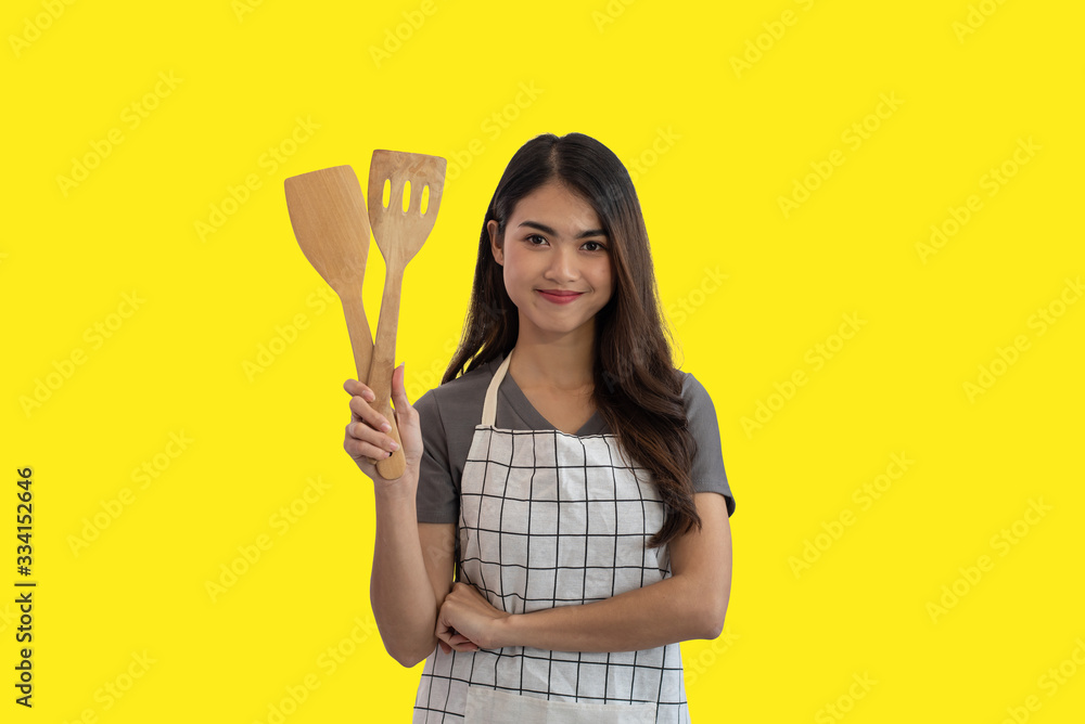 Young Asian housewife holding a wooden spatula isolated on yellow studio background Young Asian housewife holding a wooden spatula isolated on yellow studio background