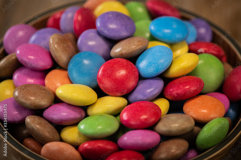 Colorful candies in a wooden bowl case isolated on wood background Colorful candies in a wooden bowl case isolated on wood background