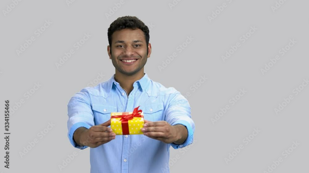 Happy cheerful dark-skinned guy giving present gift box. Portrait of hindu man holding a gift, grey isolated background. Happy cheerful dark-skinned guy giving present gift box. Portrait of hindu man holding a gift, grey isolated background.