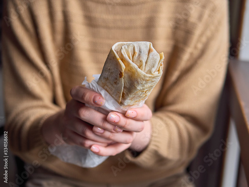 Close Up no face detail shot of woman in yellow sweater holding delicious falafel kebab roll indoors with natural window light