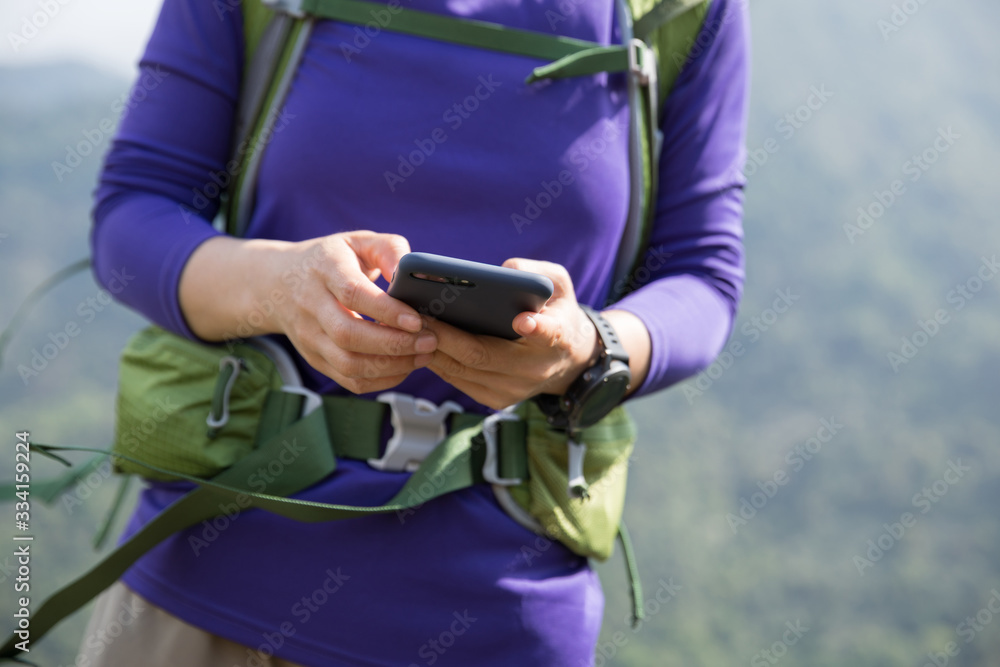Successful hiker using smartphone on mountain top cliff edge