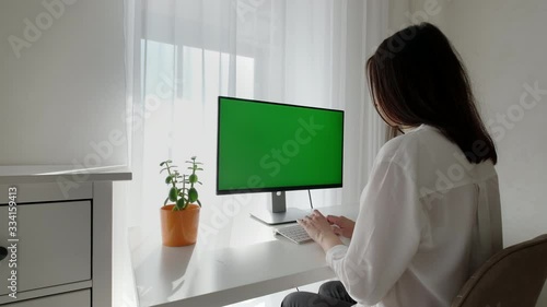 Brunette female works on her personal computer with green screen mock up display. Woman works in a modern home office