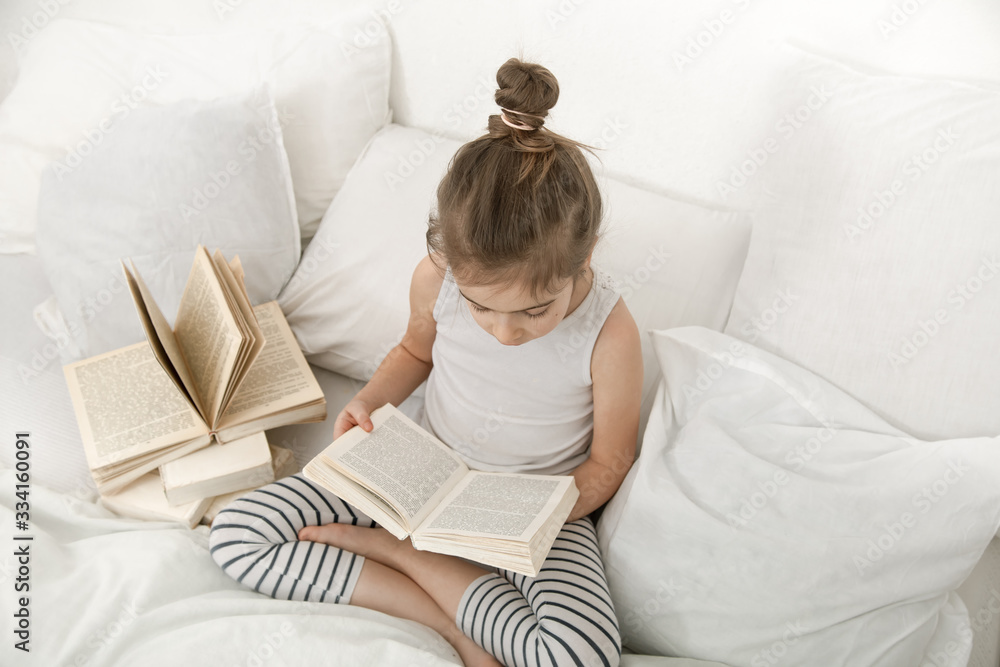 Cute little girl reading a book on the bed in the bedroom. Cute little girl reading a book on the bed in the bedroom.