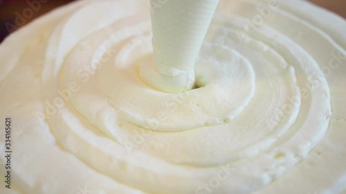 Pastry chef piping out cream filling on to a sponge cake layer using pastry bag. View from above. Close up.
