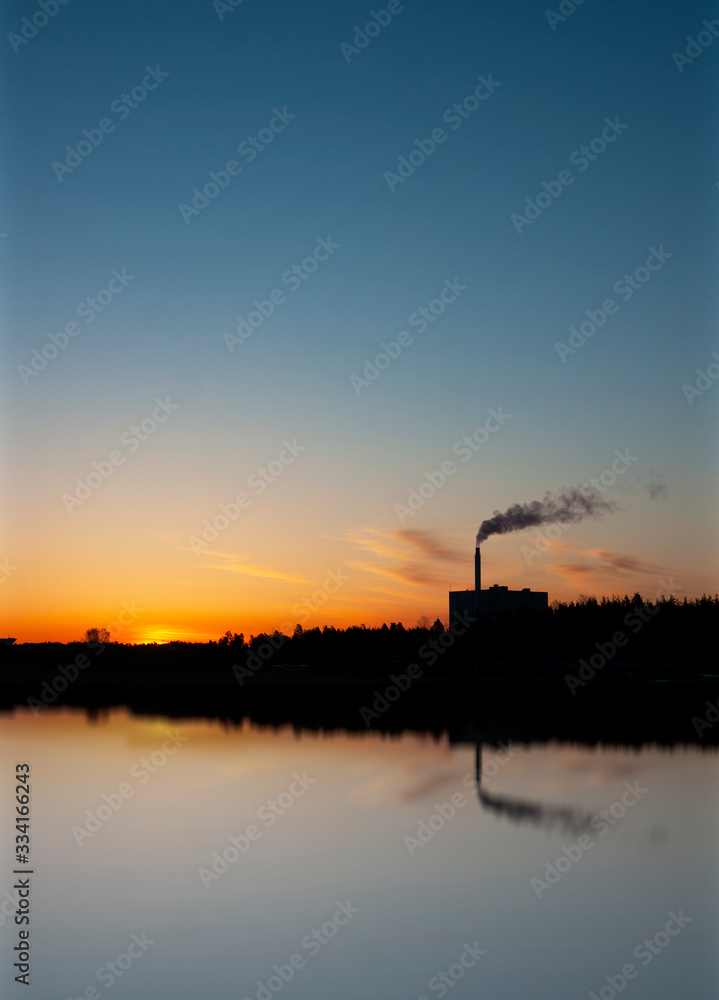 Factory or power plant at sunset, polluting the air. Reflection in water.