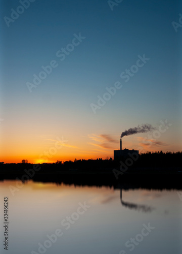 Factory or power plant at sunset, polluting the air. Reflection in water.