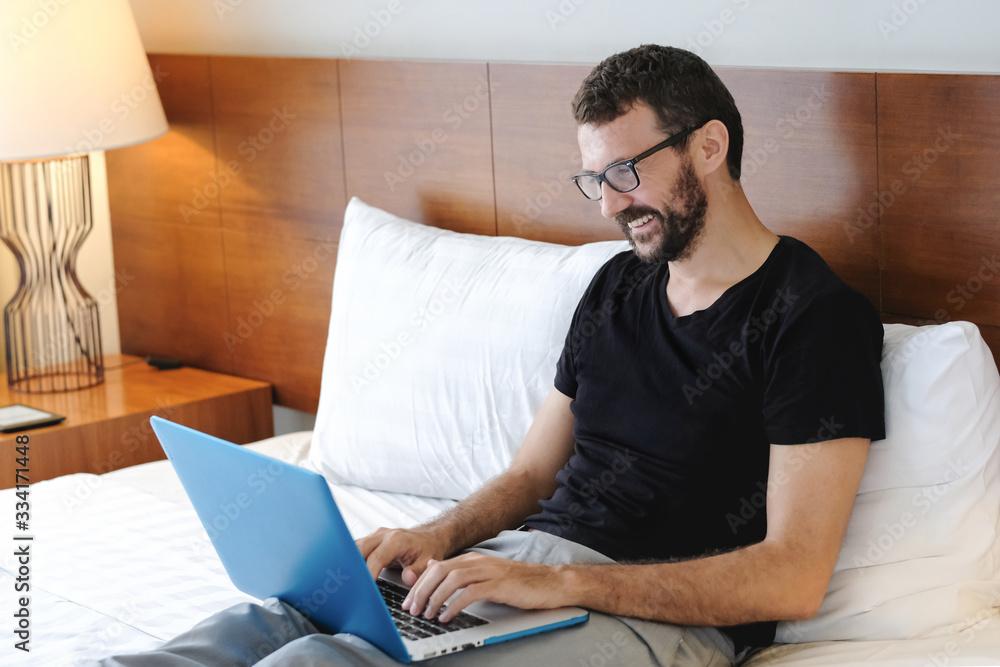 Young man is working from home during Coronavirus or Covid-19 quarantine. Man laying on bed using laptop and phone for his work during self isolation Young man is working from home during Coronavirus or Covid-19 quarantine. Man laying on bed using laptop and phone for his work during self isolation