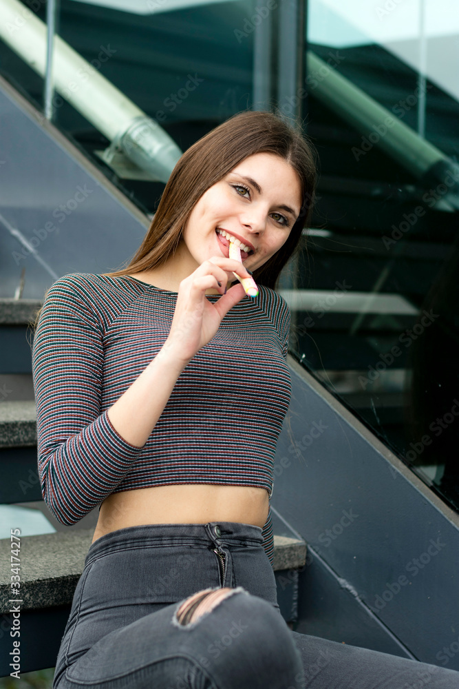 Fototapeta premium Attractive young woman with lollipop sitting on steps outdoors