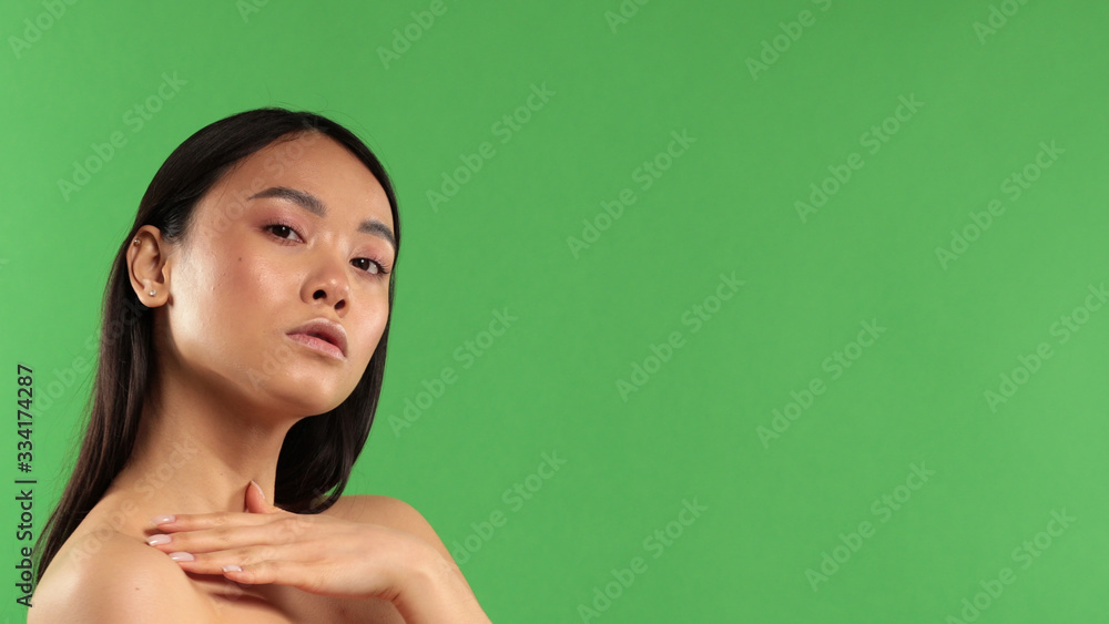 Asian girl holds hand on naked shoulder in studio on green background. Asian girl holds hand on naked shoulder in studio on green background.