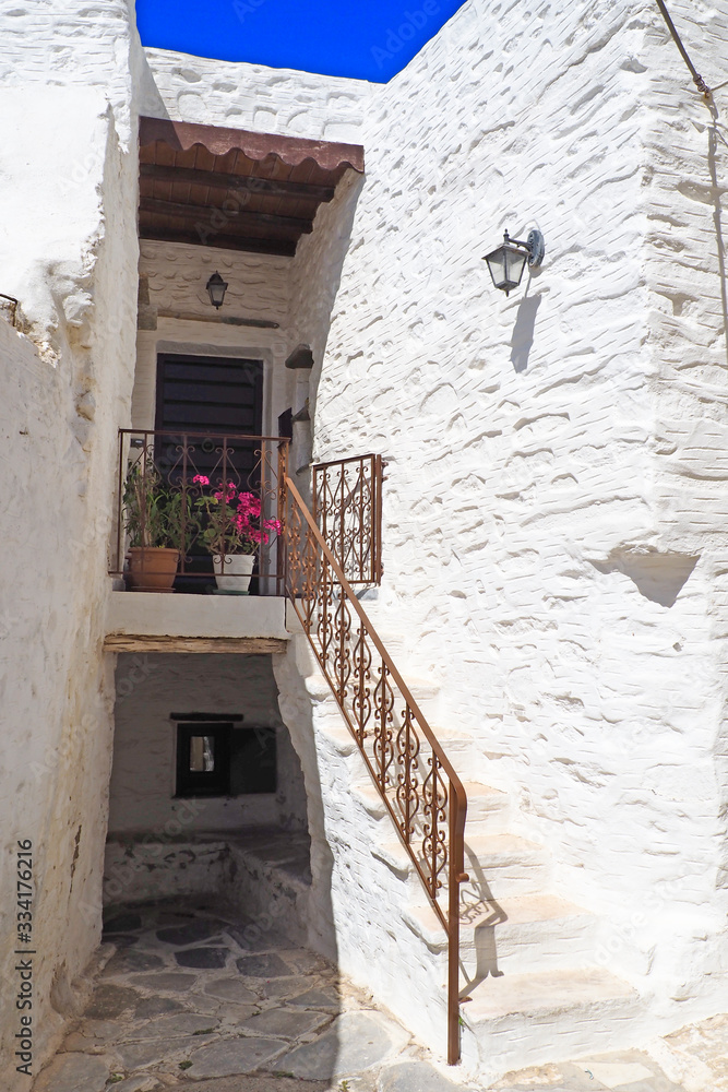 Fototapeta premium One of the charms of Mykonos, Greek island in the heart of the cyclades, are its narrow streets : white houses with small flowered balconies touching almost above paved streets