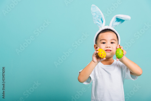 child boy wearing bunny ears and white T-shirt, standing to holds easter eggs