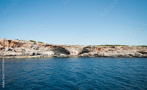 Küstenformation mit abfallender Steinpiste Felspiste vor blauem Himmel und azur blauem Meer
