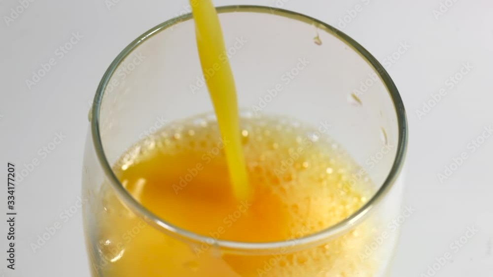 Orange juice is poured into a tall glass, on a white kitchen table with tangerines, in the kitchen. Orange juice is poured into a tall glass, on a white kitchen table with tangerines, in the kitchen.