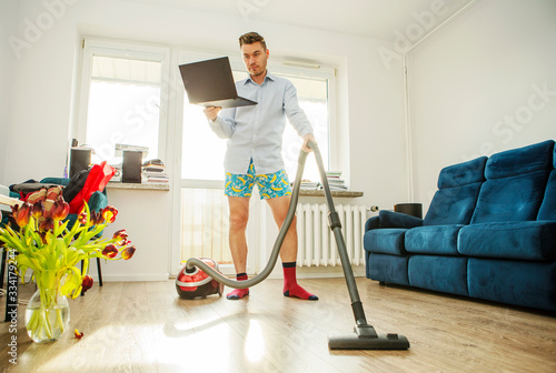 A man with a laptop and a vacuum cleaner in his apartment. Home Office
