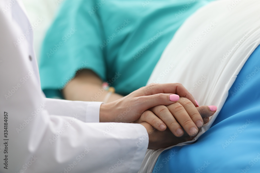 Female doctor holds sick man hospital bed by hand. Intensive care unit. Manifestations simple human attention to patients in serious condition. Help recover faster and maximize stay in intensive care Female doctor holds sick man hospital bed by hand. Intensive care unit. Manifestations simple human attention to patients in serious condition. Help recover faster and maximize stay in intensive care