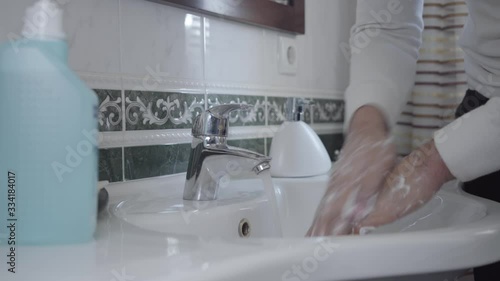 Unrecognizable tidy young man rubbing palms thoroughly with liqiud soap. Male hands washing each other in bathroom with water flowing from faucet. Health care, hygiene, coronavirus protection. photo