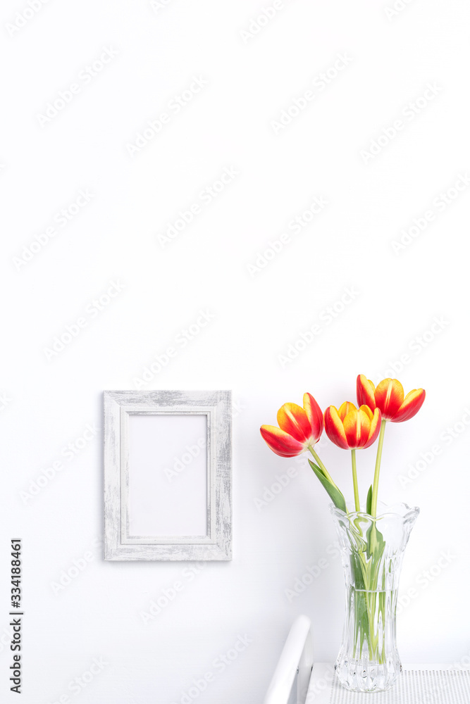 Tulip flower in glass vase with picture frame place on white wooden table background against clean wall at home, close up, Mother's Day decor concept. Tulip flower in glass vase with picture frame place on white wooden table background against clean wall at home, close up, Mother's Day decor concept.