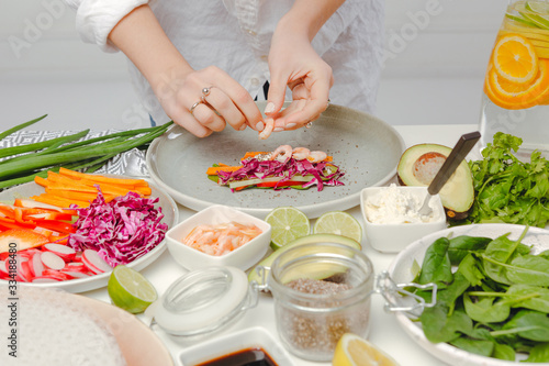 Woman's hands adding shrimps to spring roll with red cabbage, cheese, carrots, cucumbers. Delicious spring rolls with seafood.