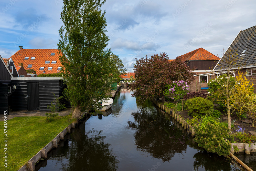 Water canal between houses in Hindeloopen in Holland. There is a boat on the water and its reflection in the water.