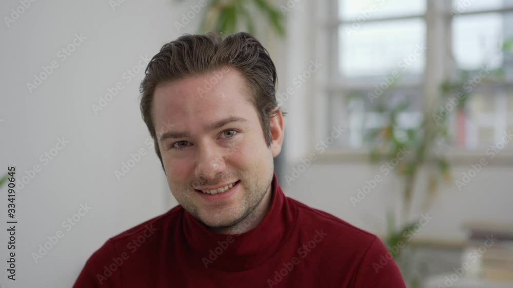 Head and shoulders portrait of handsome young man in turtleneck sweater looking at camera and smiling in office Head and shoulders portrait of handsome young man in turtleneck sweater looking at camera and smiling in office