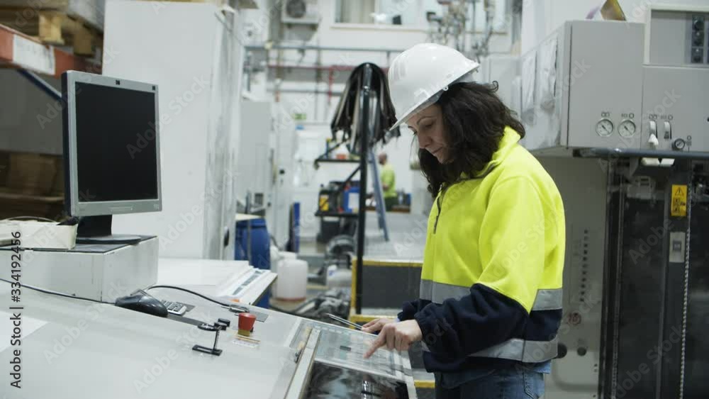 Side view of concentrated worker setting printing machine. Focused female technician working with printing machine. Manufacturing concept Side view of concentrated worker setting printing machine. Focused female technician working with printing machine. Manufacturing concept