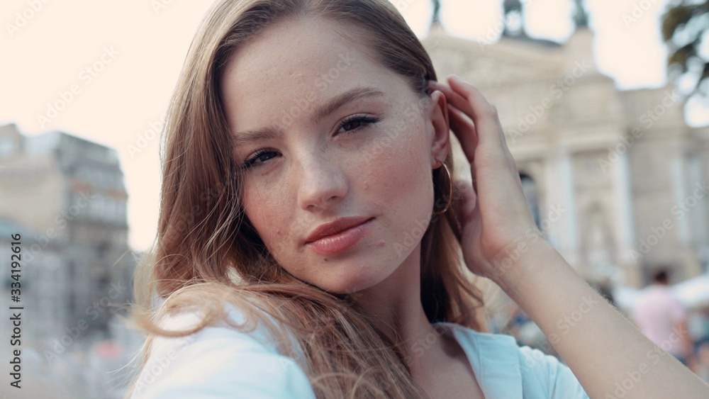 Lifestyle selfie portrait of young charming woman with curly golden hair posing and taking selfie on the street smiling and having fun Lifestyle selfie portrait of young charming woman with curly golden hair posing and taking selfie on the street smiling and having fun