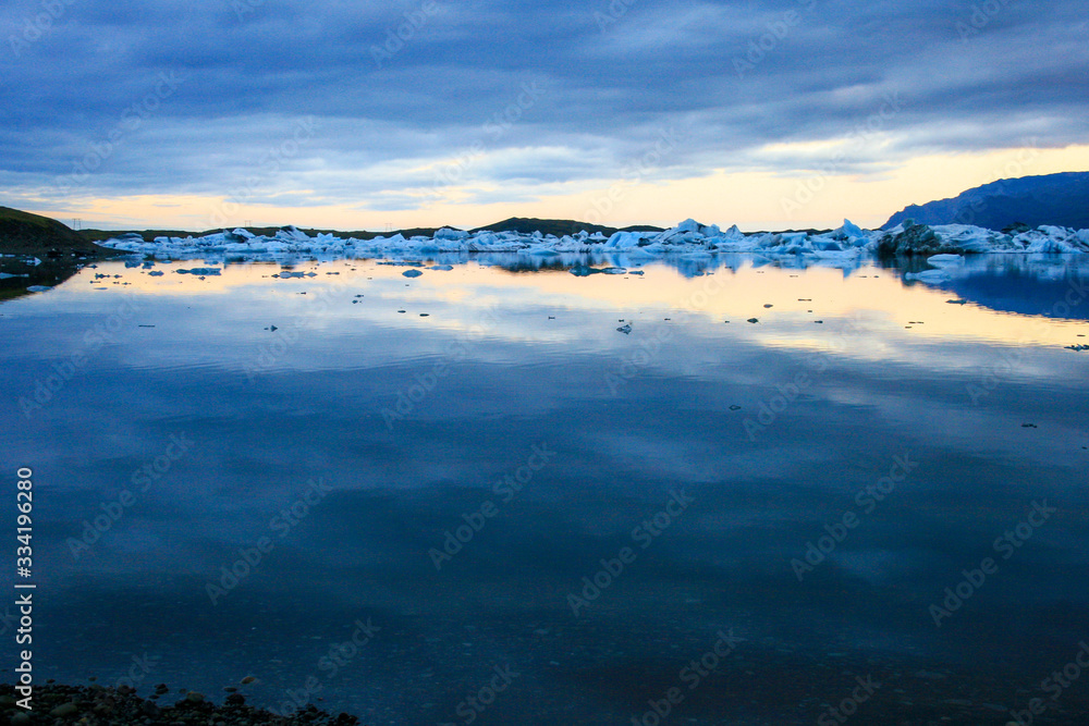 Glassy waters of Jokulsarlon glacier lagoon filled with icebergs at dawn, Iceland..