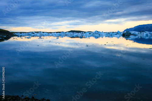 Glassy waters of Jokulsarlon glacier lagoon filled with icebergs at dawn, Iceland..