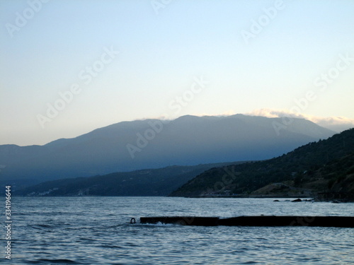 Breakwater on the shore of a calm sea against the background of coastal mountains in the haze of the sky in the distance in the evening.