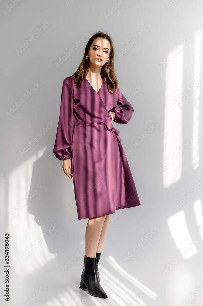 Attractive brown-haired woman in a purple checkered dress on a white background. Photosession for a clothing catalog Attractive brown-haired woman in a purple checkered dress on a white background. Photosession for a clothing catalog