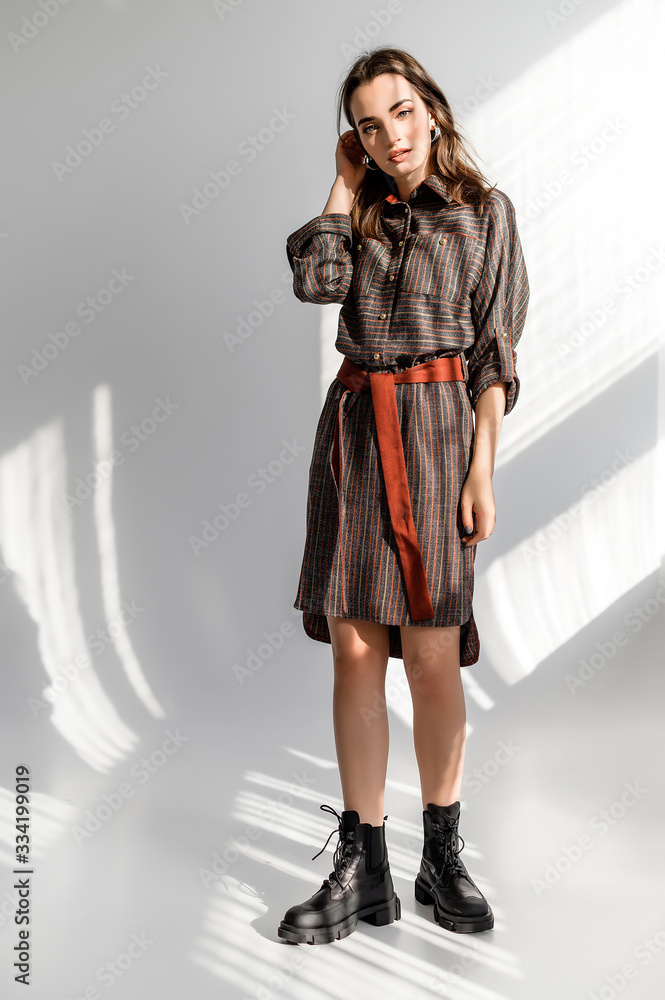 Attractive brown-haired woman in a gray checkered dress on a white background. Photosession for a clothing catalog Attractive brown-haired woman in a gray checkered dress on a white background. Photosession for a clothing catalog