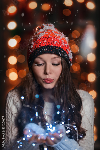 girl in winter red hat holds a garland in her hands and blows on the snow