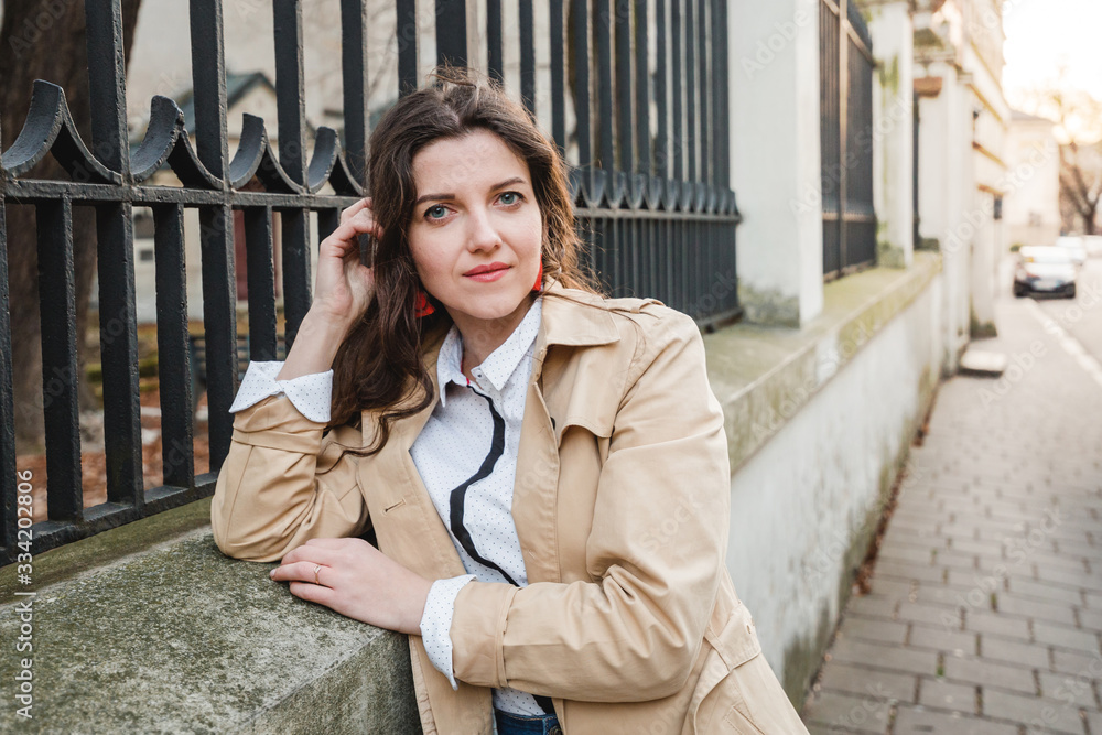 Beautiful young woman at city street. Happy tourist girl walking outdoors. Spring fashion portrait of pretty brunette female posing in old town. Beautiful young woman at city street. Happy tourist girl walking outdoors. Spring fashion portrait of pretty brunette female posing in old town.