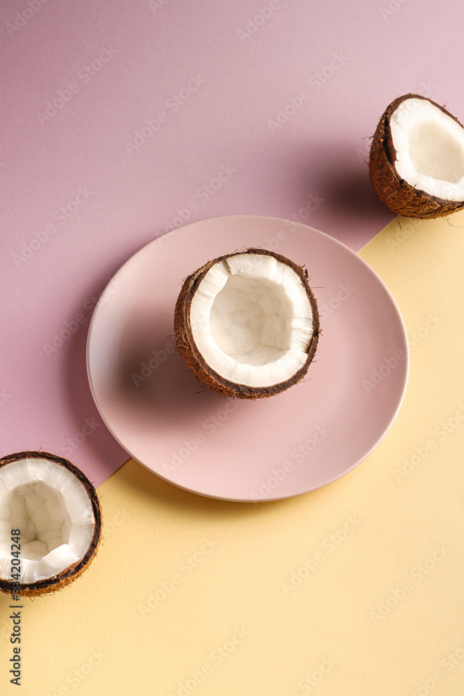Coconut half in plate with nut fruits on cream yellow and pink plain background, abstract food tropical concept, angle view Coconut half in plate with nut fruits on cream yellow and pink plain background, abstract food tropical concept, angle view