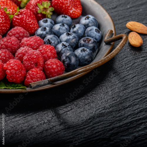 Tray with ripe organic bilberry raspberry strawberry and almonds set on slate closeup