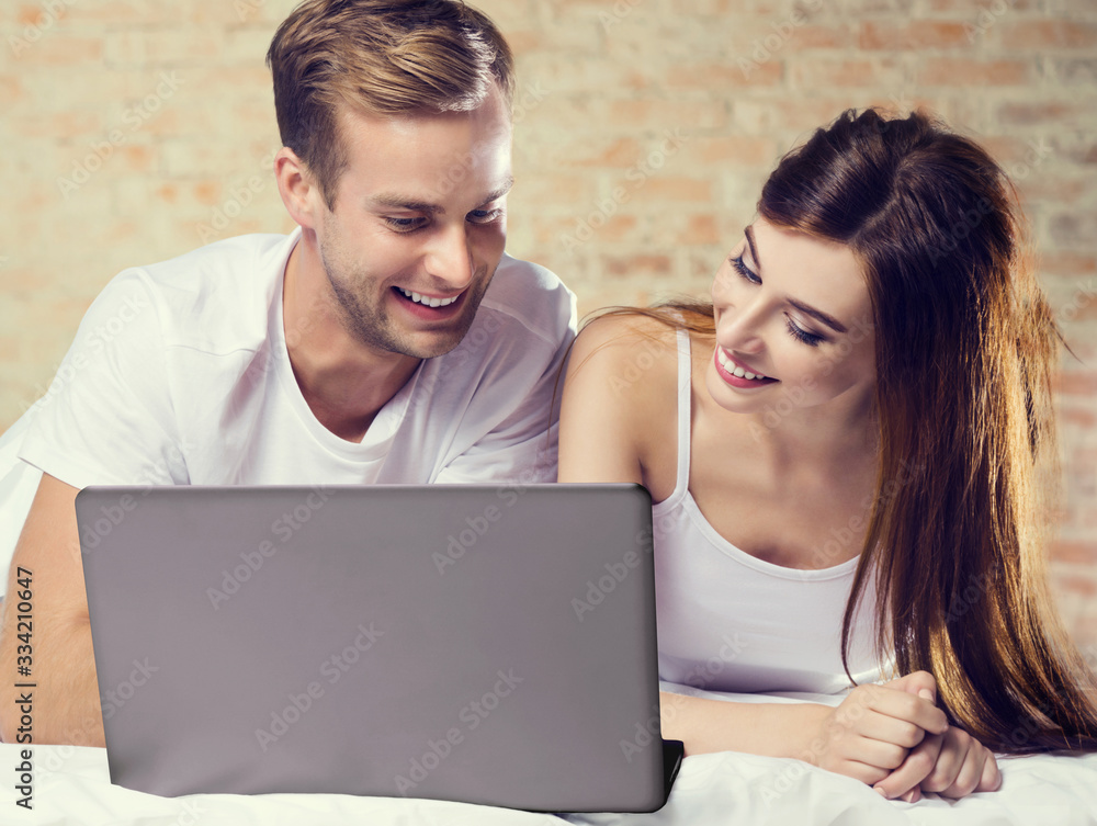 Attractive young amorous couple using laptop, on bed. Internet, technology, family, love, relationship concept photo.