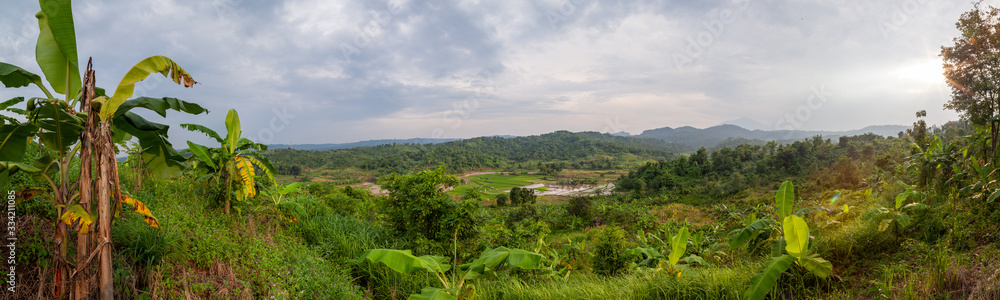 Overlooking a valley with banana trees and a small river and paddy fields. In the distance volcanos are visible. Rainy season impression in the vicinity of Semarang, Central Java.