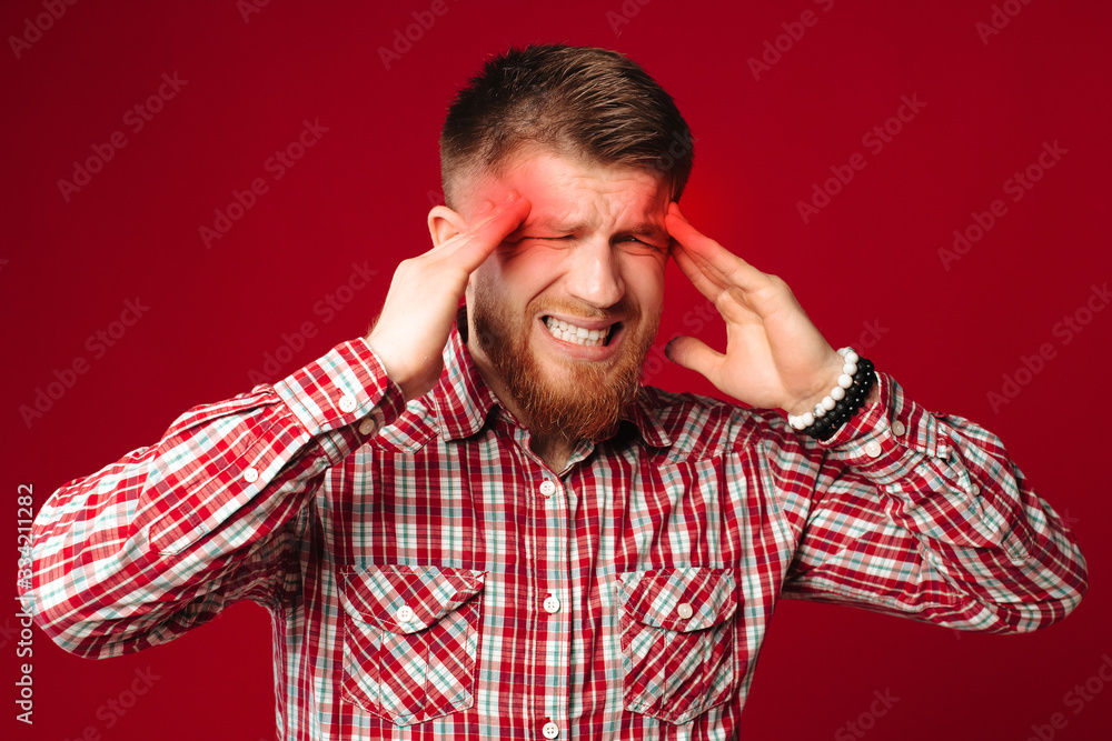 Tired young bearded man checked shirt has a headache. Redhead man holding hands on head, suffering. Tired young bearded man checked shirt has a headache. Redhead man holding hands on head, suffering.