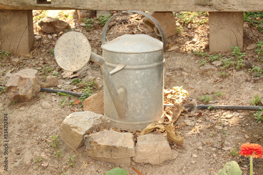 Old and rusty watering can on the stones at a garden. Old and rusty watering can on the stones at a garden.