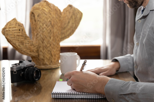 Man writing in a notebook, coffee cup and camera in the background photo camera in the background