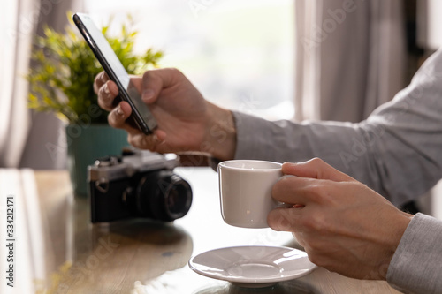 Man with a coffee cup in one hand and a cell phone in the other. photo camera in the background